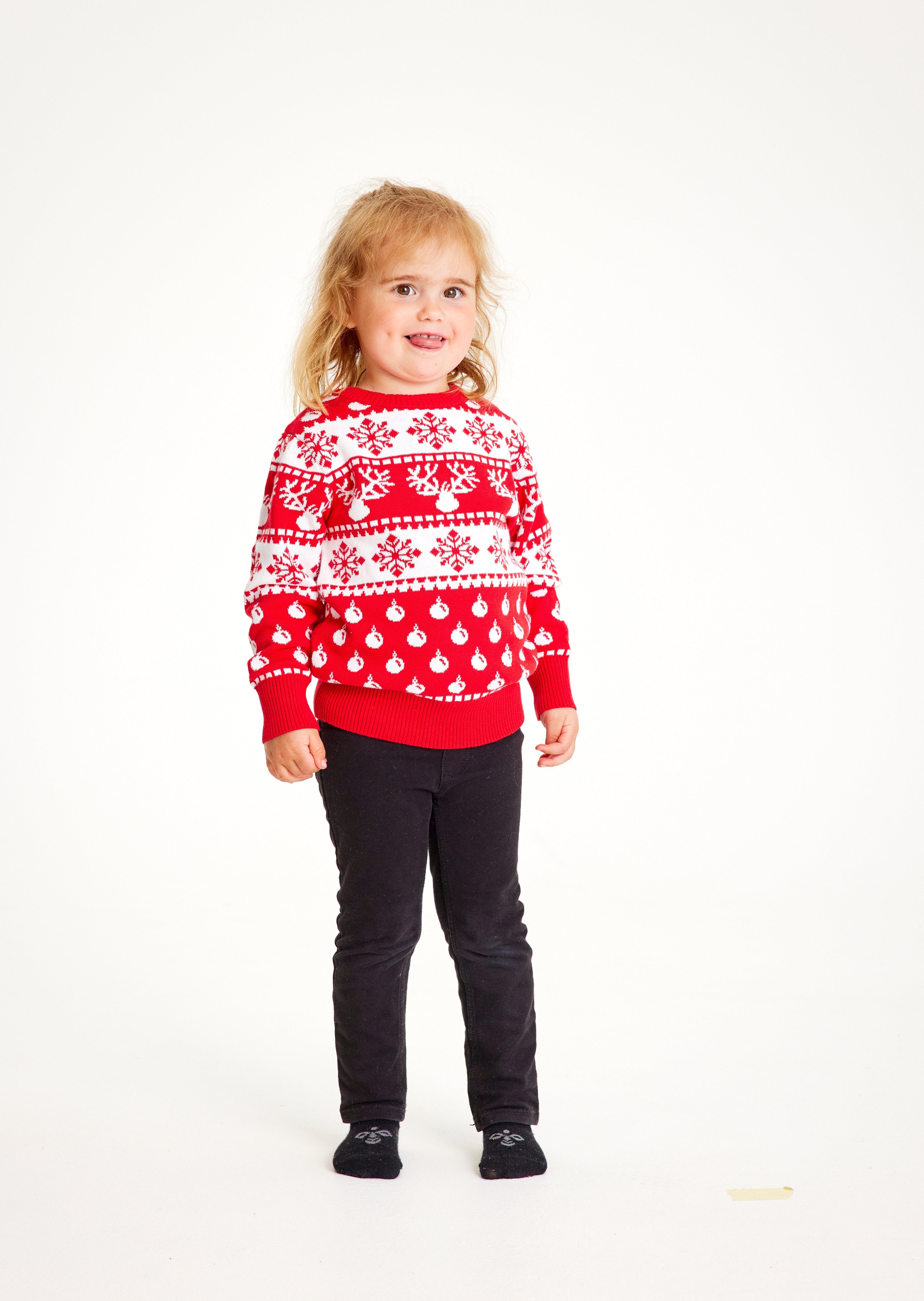 Et barn med rød julegenser med julemønster og reinsdyr.